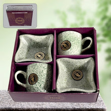 Set of ceramic mugs and trays with speckled design and logo in a purple box.