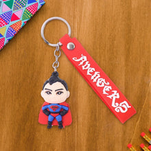 Superman keychain with red bandana and 'Avengers' text on a wooden surface