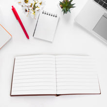 Open notebook on a white surface with a red pen, laptop, and decorative items.