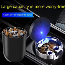 Car ashtray with blue light indicator and cigarette butts inside, placed on a car's cup holder.