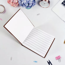 Open notebook on a desk with stationery items and flowers