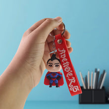 Hand holding a keychain with an 'Avengers' character against a blue background