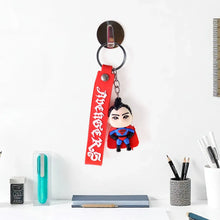 Superman keychain with red strap on a white surface with stationery items.