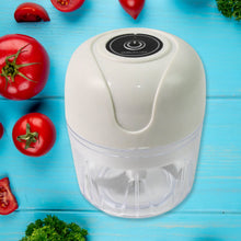 White handheld food chopper on a blue wooden surface with tomatoes and herbs around it.