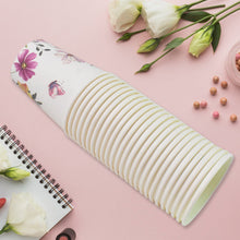 Roll of paper with floral design on a pink surface with flowers and a notebook.