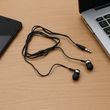 Black earbud headphones on a wooden surface with a smartphone and laptop