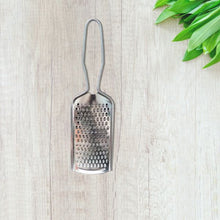 Metal grater on a light wooden surface with green leaves in the corner