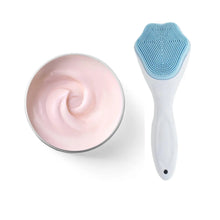 Cleansing brush with blue silicone head next to a jar of pink cream on a white background