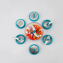 Multifunctional kitchen tool with various attachments and chopped vegetables on a light gray background