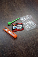 Small items including a green tool, orange tool, and a small box on a dark surface