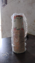 Stack of paper cups with floral design wrapped in plastic on a dark surface.