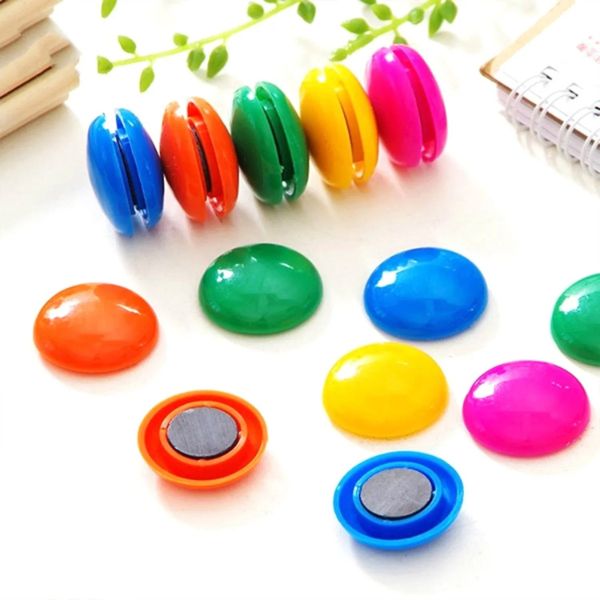 Colorful magnetic buttons on a white surface with green leaves in the background