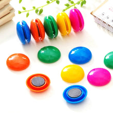 Colorful magnetic buttons on a white surface with green leaves