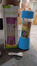 Portable blender with blue lid and charging cable next to its packaging on a concrete floor.