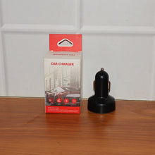 Black car charger next to its packaging on a wooden surface with a white paneled wall background.