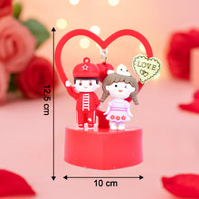 Decorative figurine of a couple with a heart and 'LOVE' text, surrounded by roses on a pink background.