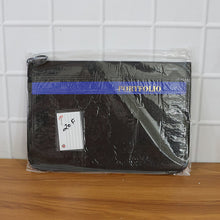 Black portfolio in clear plastic packaging on a wooden surface with a tiled wall background