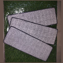 Three gray microfiber cleaning pads on a green surface
