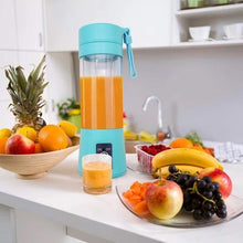 Turquoise portable juicer with orange juice on a kitchen counter with fruits