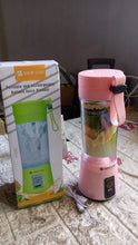 Pink portable blender with colorful juice on a tiled floor next to its packaging.